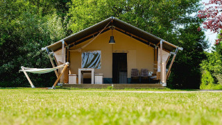 Tienda safari Villatent Nomad en Vakantiepark de Twee Bruggen, Países Bajos, rodeada de árboles y césped.