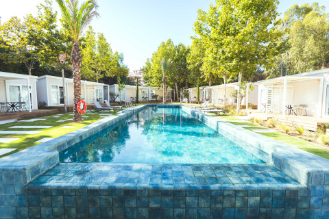 Piscina exterior rodeada de bungalows modernos y césped en Camping Costa del Sol Glamping Village, Andalucía.