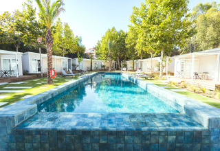 Piscina exterior rodeada de bungalows modernos y césped en Camping Costa del Sol Glamping Village, Andalucía.