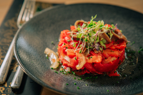 Ensalada colorida de tomates, cebollas y hierbas en un plato negro del Camping Costa del Sol Glamping Village en Andalucía.