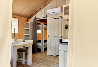 Interior view of a safari tent, Villatent Outback, featuring wooden furniture and bunk beds at Camping Village Baia Blu La Tortuga, Italy.