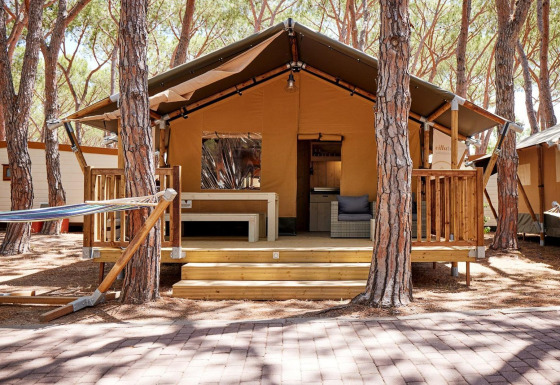 Tienda safari Villatent Outback entre pinos, con terraza de madera, hamaca y acogedor ambiente exterior.