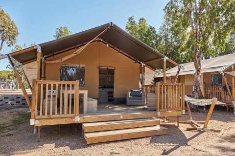 Tienda glamping en Villatent Outback con porche de madera, muebles de exterior y hamaca entre árboles.