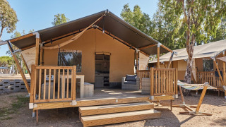 Glamping tent bij Villatent Outback met houten terras, loungezetel en hangmat in een groene omgeving.