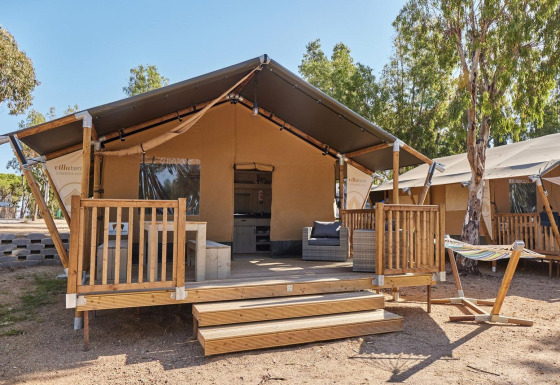 Tenda glamping al Villatent Outback con veranda in legno, poltrone da esterno e amaca tra gli alberi.