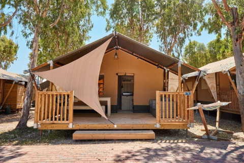 Tienda safari Villatent Outback en Camping Laguna Blu en Italia, con terraza de madera y hamaca exterior.