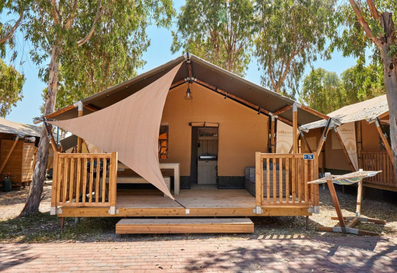 Tienda safari Villatent Outback en Camping Laguna Blu en Italia, con terraza de madera y hamaca exterior.