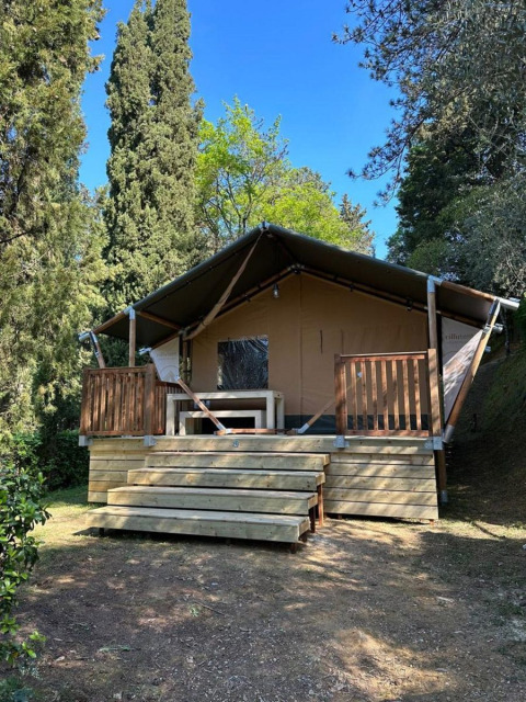 Tienda safari Villatent Wood en Camping Colleverde, Italia, rodeada de árboles y naturaleza bajo cielo azul.