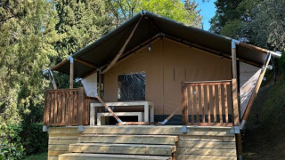 Tienda safari Villatent Wood en Camping Colleverde, Italia, rodeada de árboles y naturaleza bajo cielo azul.