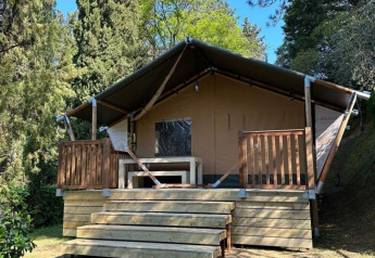 Tienda safari Villatent Wood en Camping Colleverde, Italia, rodeada de árboles y naturaleza bajo cielo azul.