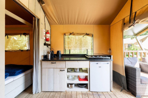 Interior de la tienda safari Villatent Wood en Camping Nautic Almata con cocina pequeña y zona de dormir.