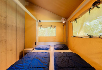 Vue intérieure de la tente safari Villatent Wood avec deux lits et du linge bleu au Camping Nautic Almata.