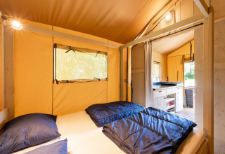 Vista interior de una tienda safari con cama cómoda y cocina sencilla en Camping Nautic Almata, España.
