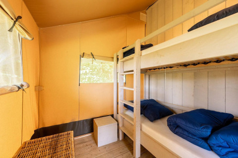 Interior de una tienda safari en Camping Nautic Almata, España, con literas y mobiliario sencillo de madera.