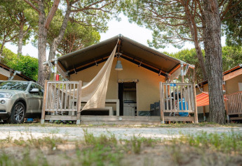 Villatent Outback safari tent with porch, car parked beside, set among tall pine trees in nature.