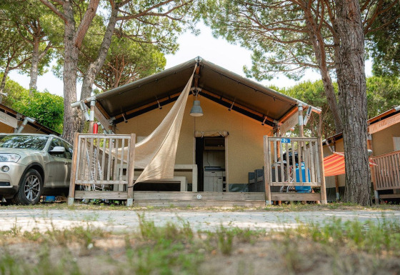 Villatent Outback safari tent with porch, car parked beside, set among tall pine trees in nature.