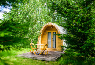 Kleine Holzhütte mit Terrasse und Gartenmöbeln, umgeben von grünen Bäumen auf Netl Camping Kallumaan, Niederlande.
