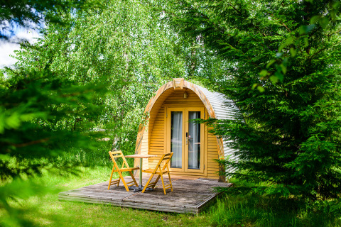Petite cabane en bois avec terrasse et chaises de jardin entourée de verdure à Netl Camping Kallumaan, Pays-Bas.