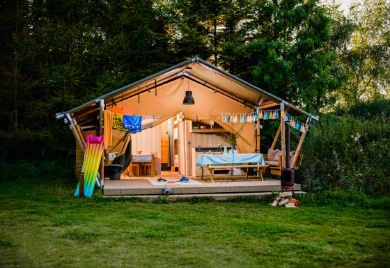 Safaritent Lodge + sanitary Leri - UFO met veranda, picknicktafel en kleurrijke slinger in het groen.