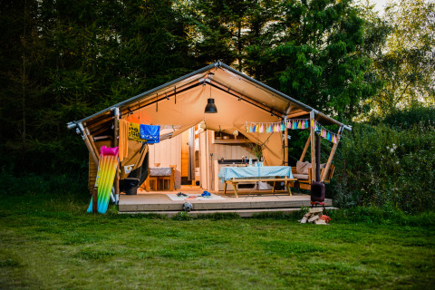 En safaritelte kaldet Lodge + sanitary Leri - UFO med hyggelig veranda, bord og farverig dekoration i naturen.