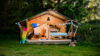 Safari tent named Lodge + sanitary Leri - UFO with a veranda, colorful banner, and outdoor dining area.
