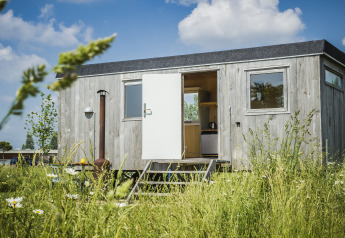 Pipowagen tiny house at Netl Camping Kallumaan in the Netherlands, surrounded by tall grass and wildflowers.