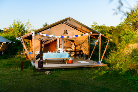 Safaritent Lodge Stuga - HELI op Netl Camping Kallumaan in Nederland, met tafel en gezellige veranda.
