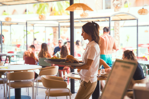 En tjener serverer mad til gæster på en solrig glamping-restaurant i Camping Costa del Sol, Andalusien.