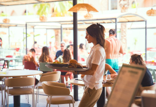 Eine Kellnerin serviert Speisen in einem sonnigen Restaurant im Camping Costa del Sol Glamping Village, Andalusien.