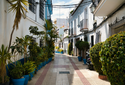 Callejón estrecho en Fuengirola, Andalucía, España, con casas blancas y muchas plantas en macetas azules.
