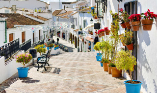 Calle colorida cerca de Fuengirola, Andalucía, con casas blancas, flores en macetas y bancos bajo el sol.