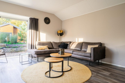 Sala moderna en la cabaña Velthorst de De Wije Werelt, Países Bajos, con sofá esquinero y ventana grande.