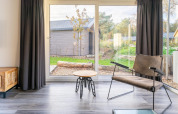 Sala luminosa en la cabaña Velthorst de De Wije Werelt, Países Bajos, con vista al jardín y mobiliario moderno.