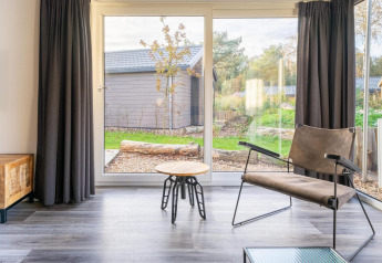 Lys stue i Velthorst lodge på De Wije Werelt med store vinduer, moderne stol og udsigt til haven.