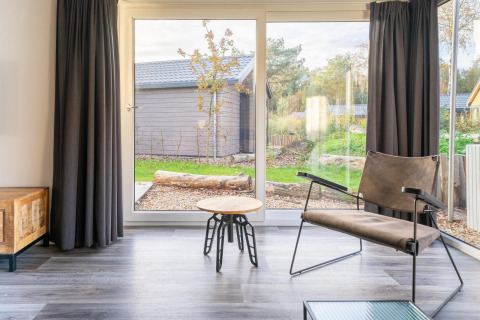 Sala luminosa en la cabaña Velthorst de De Wije Werelt, Países Bajos, con vista al jardín y mobiliario moderno.