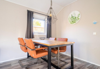 Moderne spisestue med træbord, orange stole og stort vindue på Velthorst-lodgen, De Wije Werelt, Holland.
