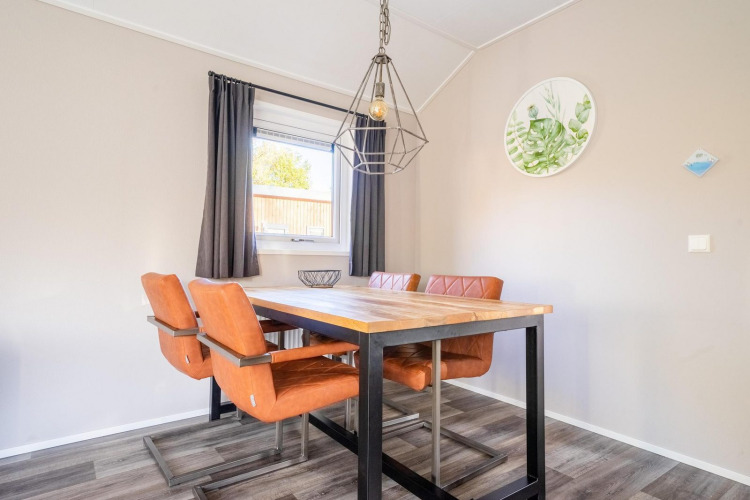 Comedor moderno con mesa de madera, sillas naranjas y ventana en la cabaña Velthorst, De Wije Werelt, Países Bajos.