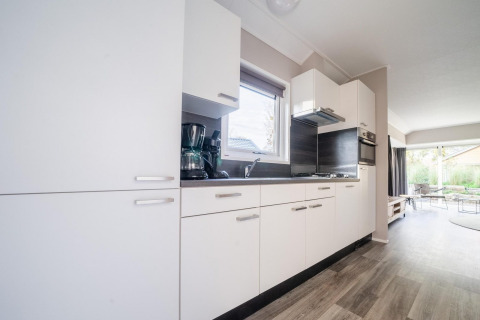 Modern kitchen in a Velthorst lodge at De Wije Werelt, Netherlands, with white cabinets and garden view.