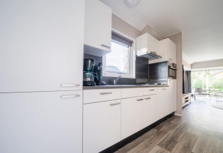 Modern kitchen in a Velthorst lodge at De Wije Werelt, Netherlands, with white cabinets and garden view.