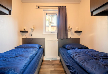 Twee eenpersoonsbedden met blauw beddengoed in de Velthorst-lodge op De Wije Werelt, Nederland, centraal gefotografeerd.