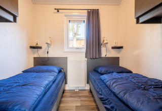 Deux lits simples avec literie bleue dans la lodge Velthorst à De Wije Werelt, Pays-Bas, vus depuis le centre de la pièce.
