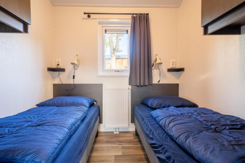 Deux lits simples avec literie bleue dans la lodge Velthorst à De Wije Werelt, Pays-Bas, vus depuis le centre de la pièce.