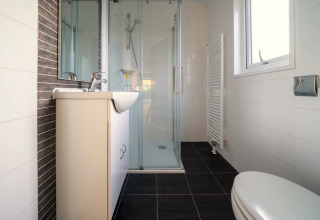 Salle de bain moderne avec douche, toilettes, lavabo et fenêtre à la Velthorst Lodge, De Wije Werelt, Pays-Bas.