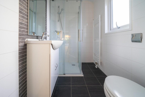 Baño moderno con ducha cerrada, inodoro, lavabo y ventana en la cabaña Velthorst de De Wije Werelt, Países Bajos.