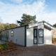 Et moderne Berkel-lodge med store vinduer, omgivet af natur og en grussti, under en klar himmel.