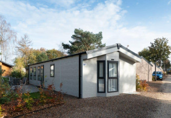 Lodge Berkel moderne avec de grandes fenêtres, dans un cadre naturel, sur sentier gravillonné sous ciel bleu.