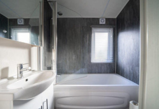 Salle de bain moderne au lodge Berkel à De Wije Werelt, Pays-Bas, avec baignoire, lavabo et fenêtre.