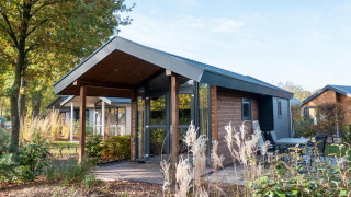Una pequeña cabaña llamada Tiny House en De Wije Werelt, Países Bajos, rodeada de naturaleza y muebles de exterior.
