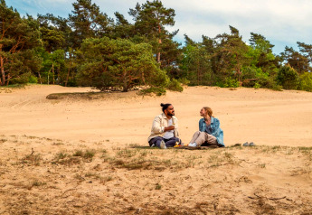 Zwei Personen machen ein Picknick auf Sand in der Natur, ein Urlaub bei einer Glamping-Unterkunft.