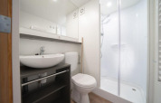 Baño moderno en Glampingtent con lavabo, inodoro y ducha amplia, diseño limpio y luminoso.